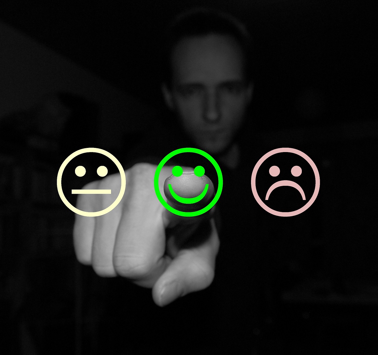 Foto de um homem sério apontando o dedo indicador pra frente, com os braços esticados. Na tela, três emojis em formato de arte. O primeiro está sem reação, o segundo está feliz e o terceiro está triste. 